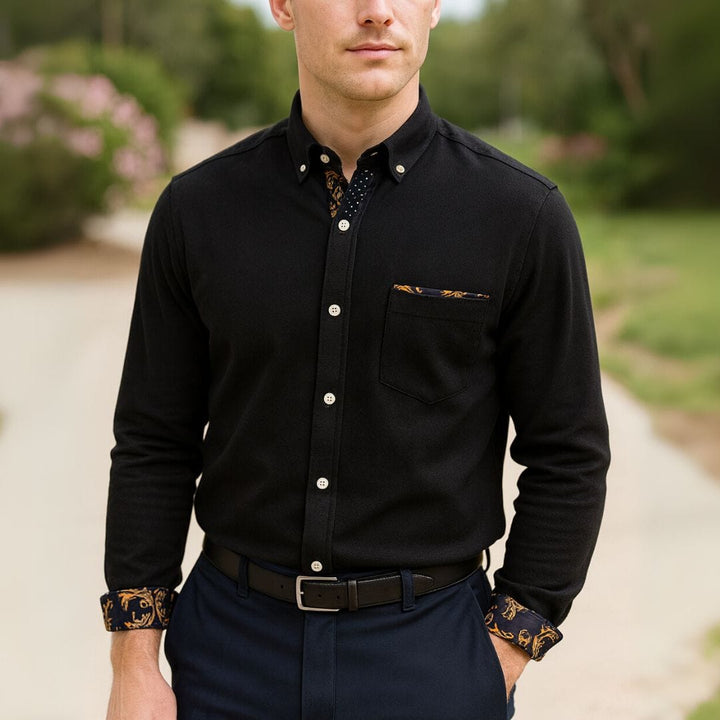Close up front view of a man wearing a black classic corduroy long-sleeve shirt with patterned cuffs and pocket square