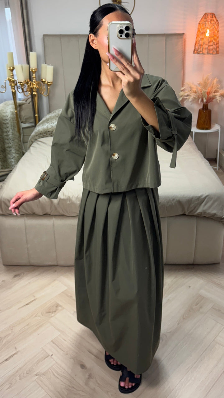 Front view, model in an olive cropped set with a pleated skirt and bow sleeves, holding a phone