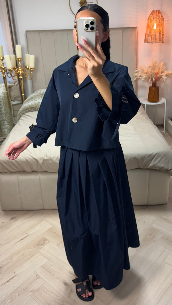 Front view, model wearing a navy cropped set with a pleated skirt and bow sleeves, holding a phone