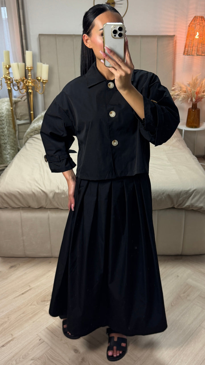 Front view, model wearing a black cropped top and a pleated skirt, holding a phone to her face