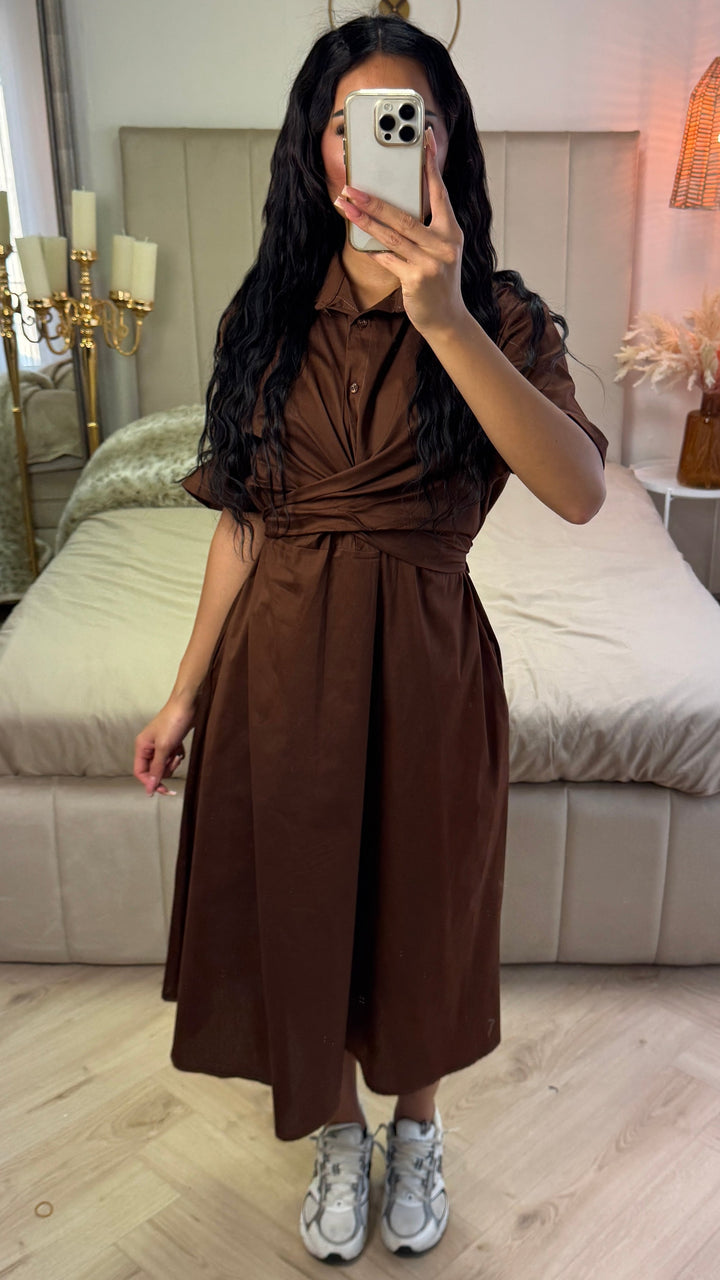 Front view, worn by model, a brown cross tie belt blouse dress in soft cotton blend with a phone covering her face