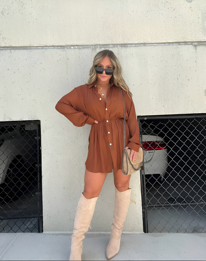 Front view, model wearing a brown satin romper with a self-tie belt and beige knee high boots