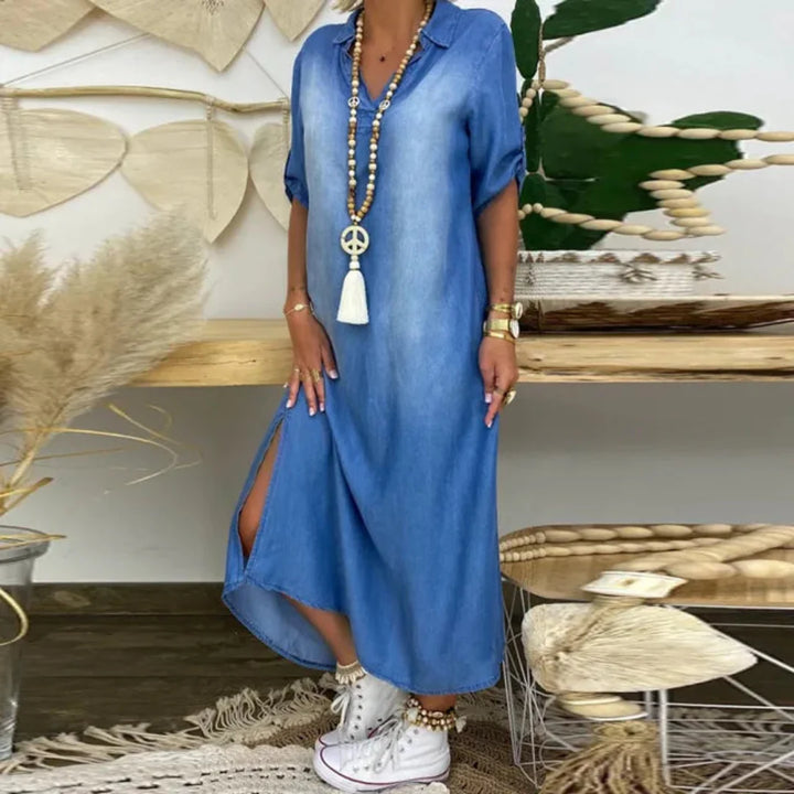 Front view of a woman wearing a blue V-neck denim dress with side splits and a long necklace