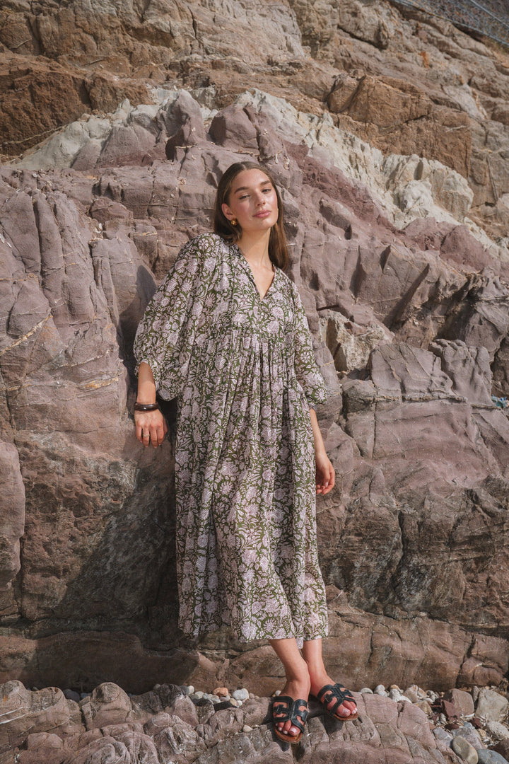 Front view, model wearing a loose fit floral summer midi dress against a rocky backdrop