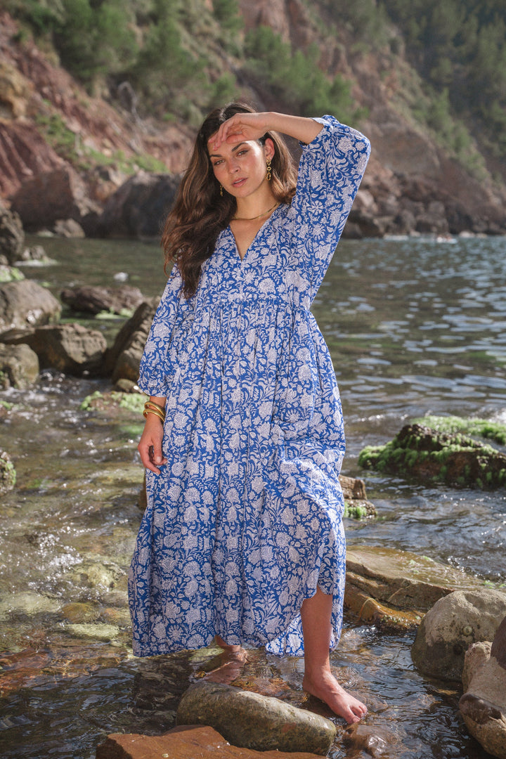 Front view, worn by model, a woman in a blue and white vintage floral dress standing in shallow water on rocks