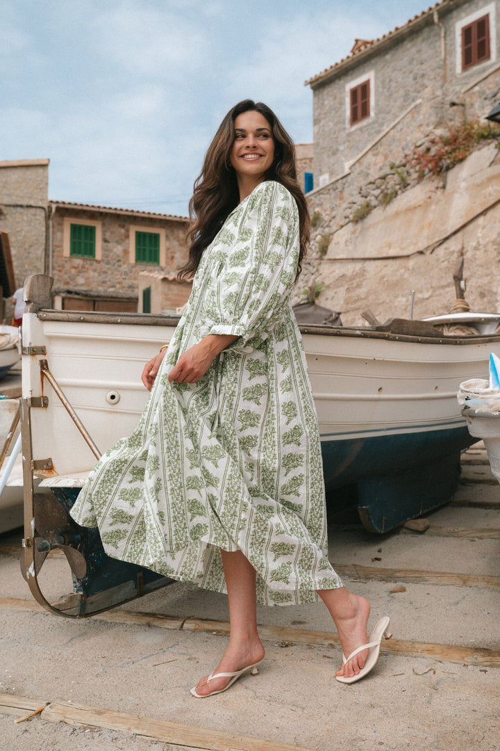 Front view of model wearing a Briana midi dress in green and white print, standing by boats on a sunny day