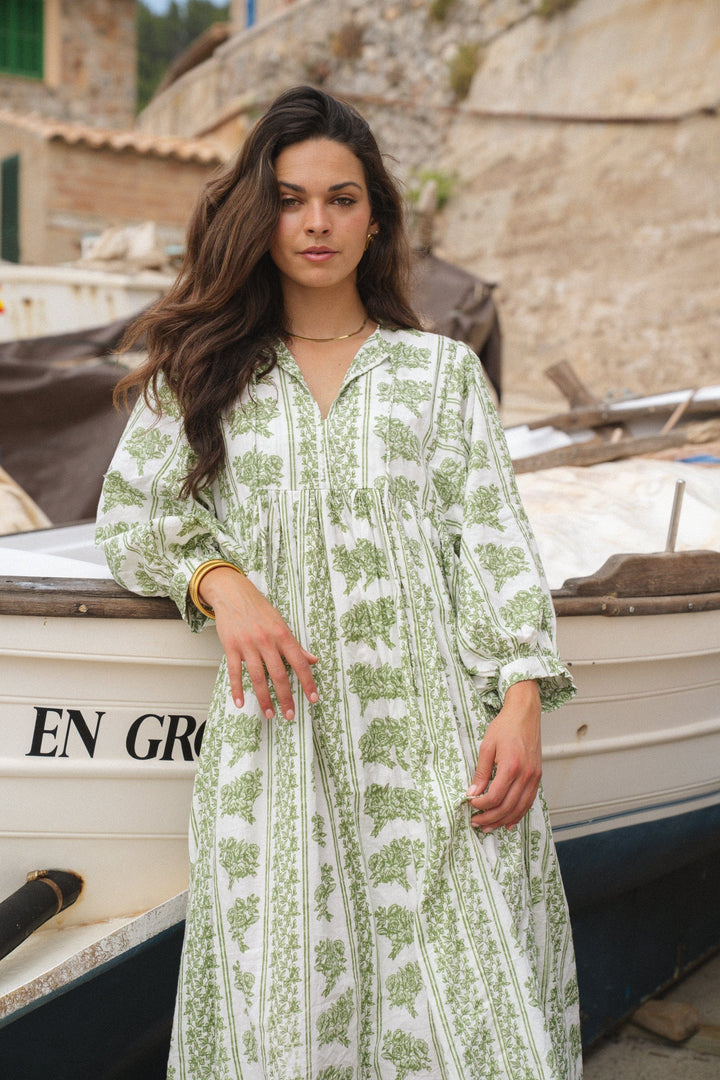 Front view of model in a Briana midi dress, leaning on a white boat with green trim details