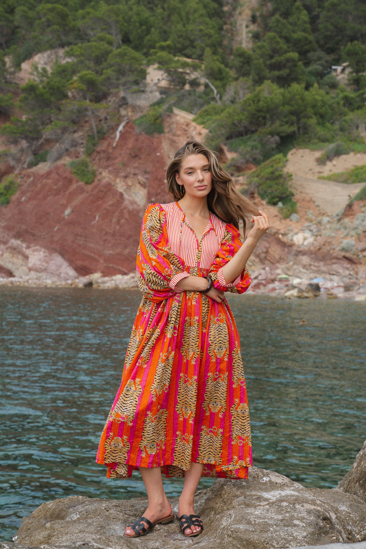 Front view of a model wearing the V-neck lantern sleeve midi dress with a floral and striped pattern by the water