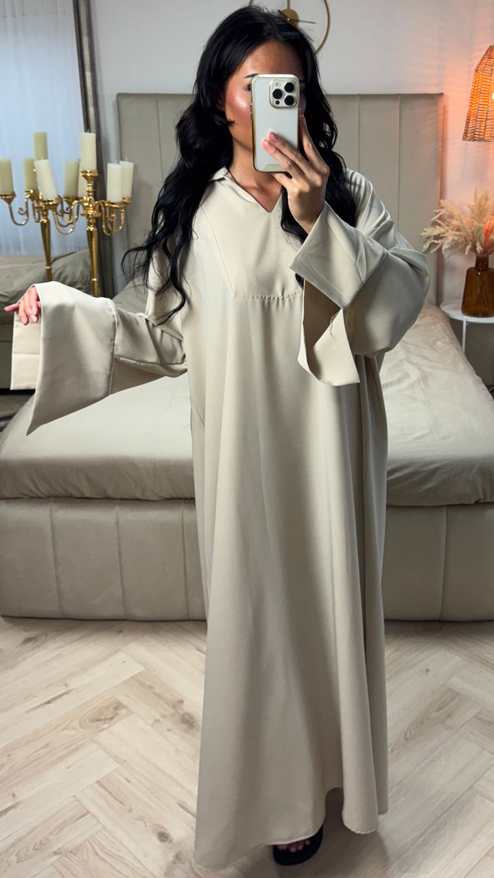 Front view of a model in a beige cotton abaya, showing the V-neck and split sleeves while holding a phone, alternate angle