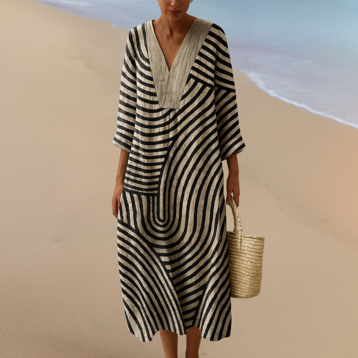 Front view of a model in a boho floral print dress with black and white stripes and a beige beach bag