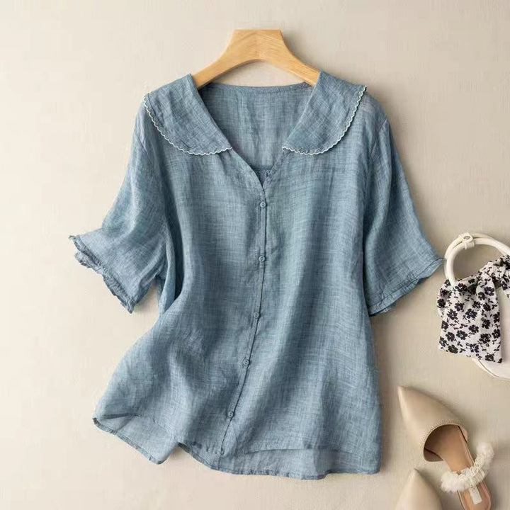 Front view of a blue lightweight linen blouse with a white scalloped collar and short sleeves on a hanger