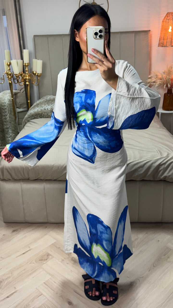 Front view of a model wearing a white floral print maxi dress with large blue flowers and elegant bow detail