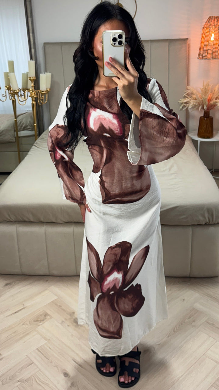 Front view of a model wearing a white floral print maxi dress with large brown flowers and flared sleeves