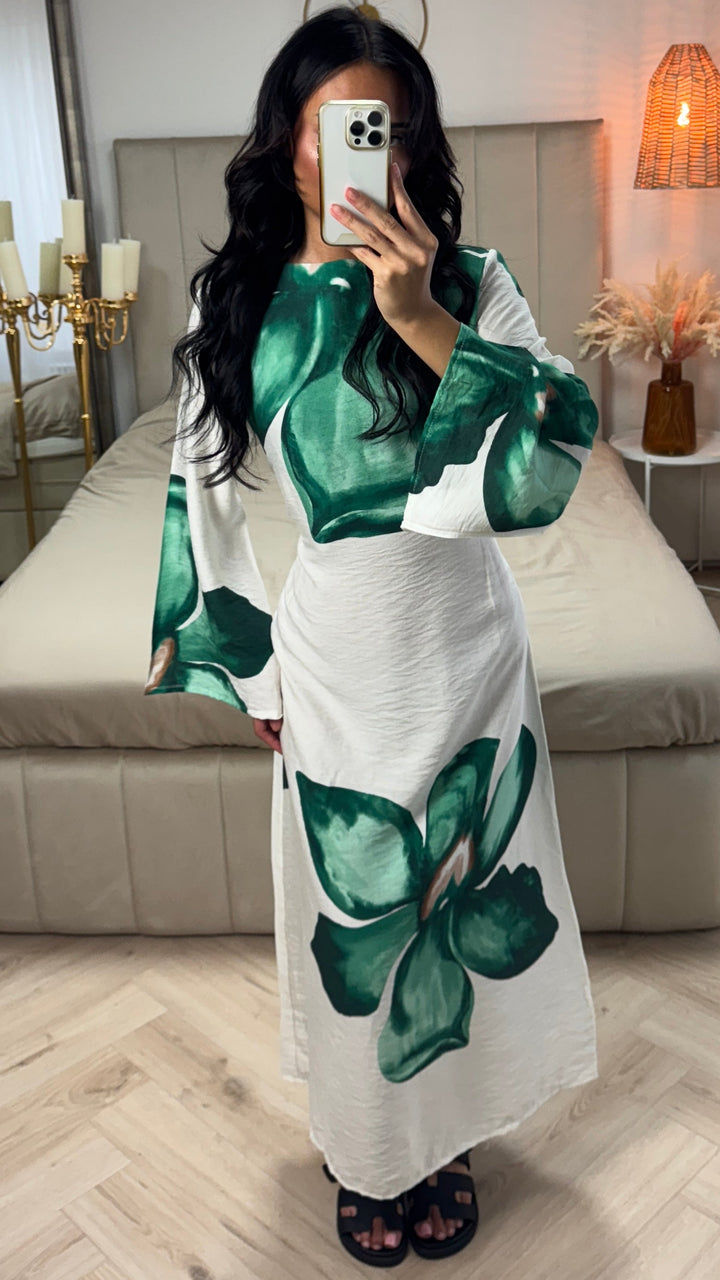 Front view of a model wearing a white floral print maxi dress with large green flowers and flared sleeves
