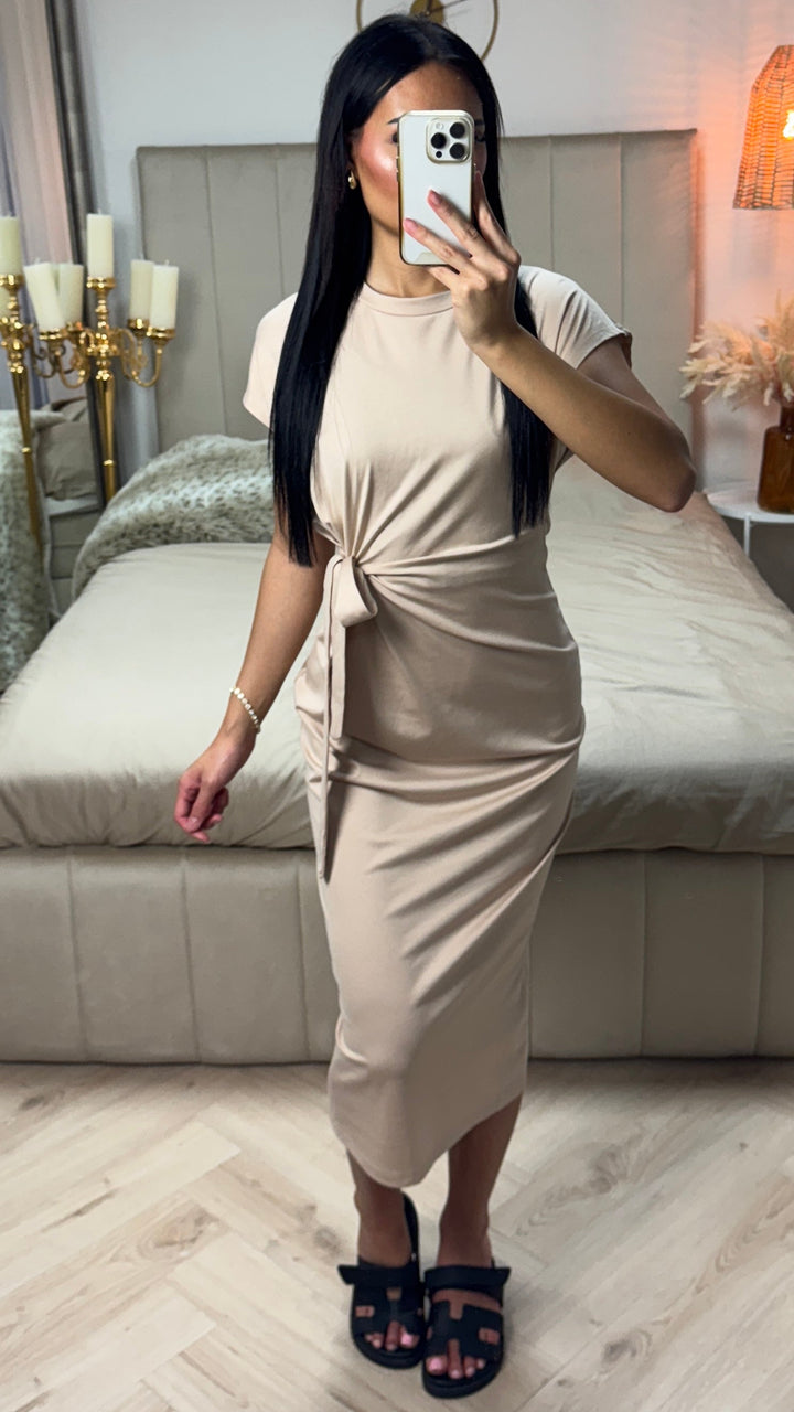 Front view of a model wearing the beige Aurora midi dress with elegant bow detail and black sandals