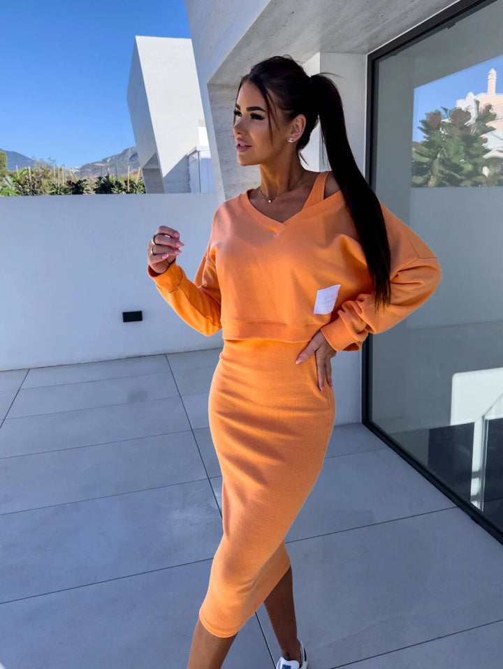 Three quarter view of a model wearing a casual orange sweatshirt and dress set with a white square patch on the top