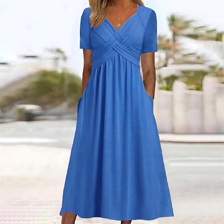 Front view of the blue Evelyn midi dress worn by a model, featuring a v-neckline and side pockets