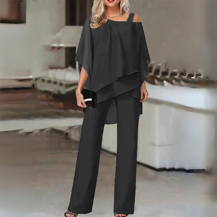 Front view, model wearing elegant straight-leg trousers and flowing top set in charcoal with black clutch and heels