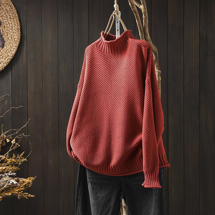Front view of a red textured knit sweater, an oversized autumn pullover hanging on a branch with dark jeans