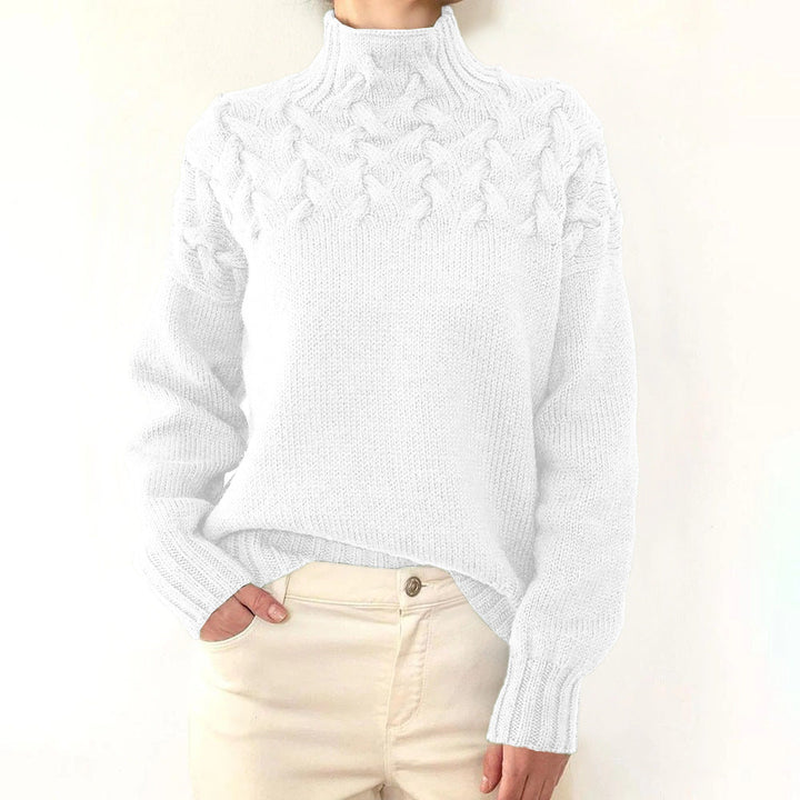 Front view of a model wearing a white cable knit mock neck sweater with cream trousers, hand in pocket