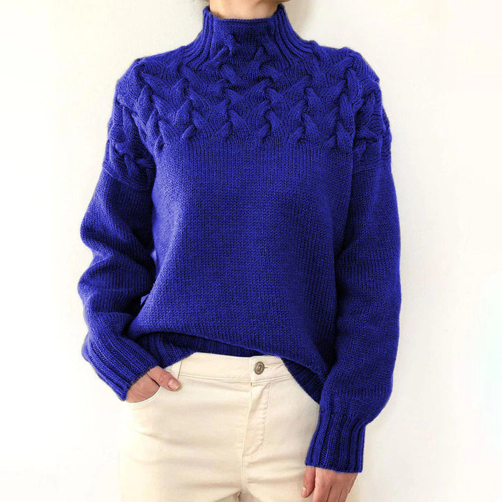 Front view of a model wearing a royal blue cable knit mock neck sweater with cream trousers, hand in pocket