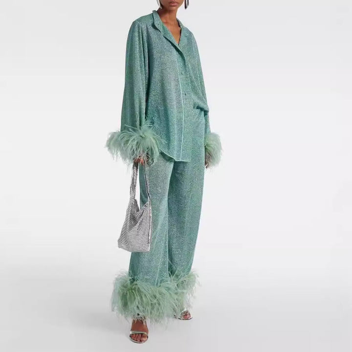 Side view, model wearing a sparkling green two-piece set with feather cuffs and feather hems, holding a silver bag