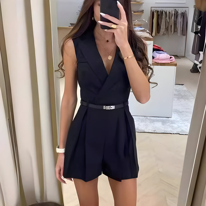 Front view of a woman wearing the black elegant summer jumpsuit with a thin black belt, taking a mirror selfie