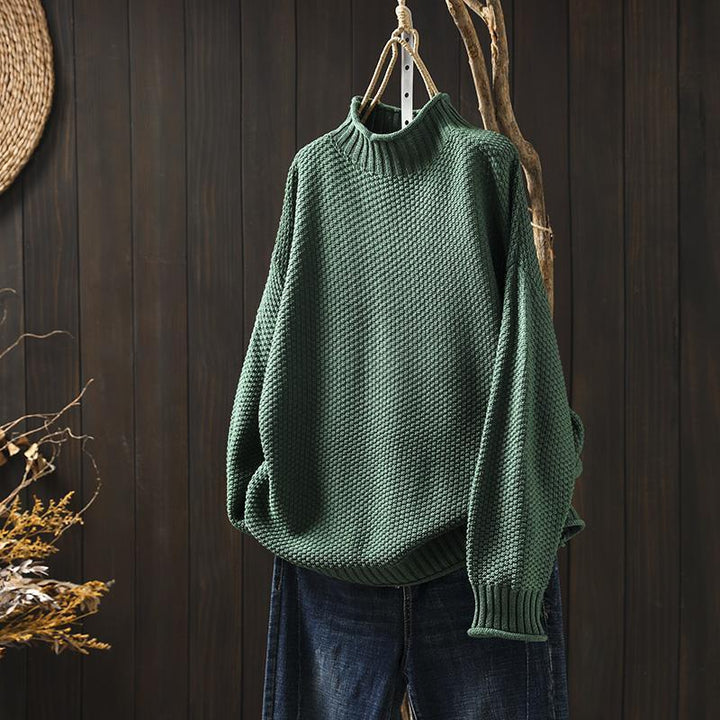 Front view of a green textured knit sweater, an oversized autumn pullover hanging on a branch with blue jeans