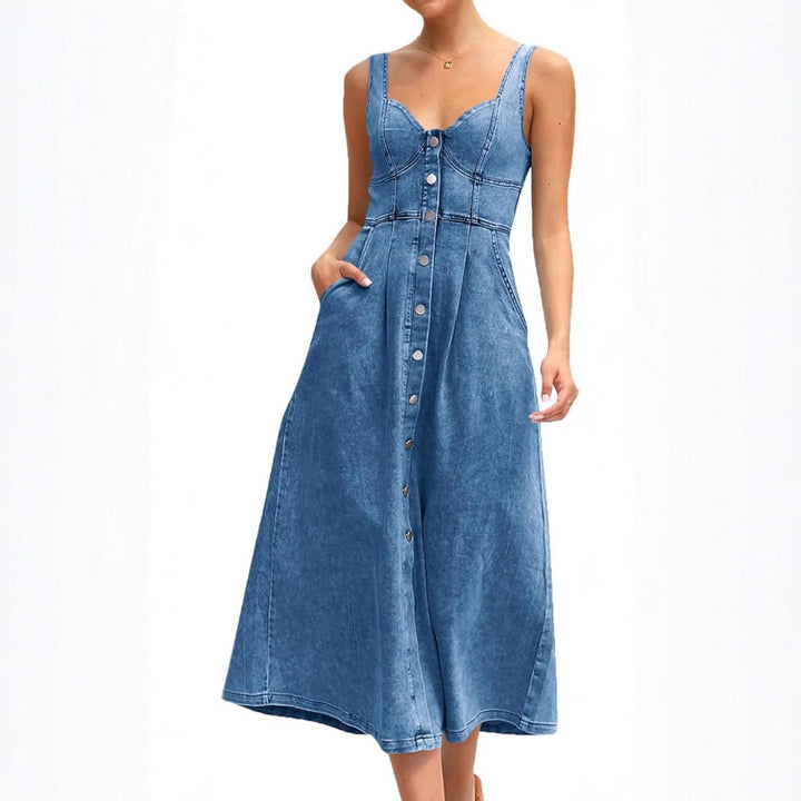 Front view of a model wearing a light blue classic sleeveless button-front denim dress with one hand in a pocket