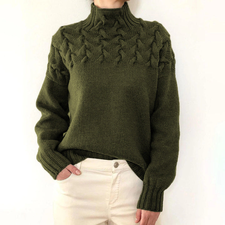 Front view of a model wearing a dark green cable knit mock neck sweater with cream trousers, hand in pocket, alternate angle