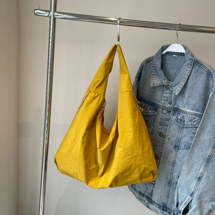 Front view of a yellow Lush Everyday Tote Bag hanging on a rail next to a denim jacket