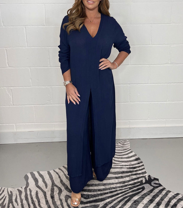 Front view of a model in a navy two-piece wide leg jumpsuit set with a long tunic top and v-neck, hand on hip