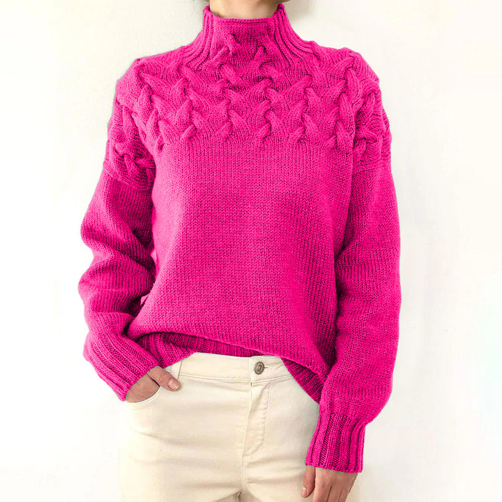 Front close up of a model wearing a pink cable knit mock neck sweater with cream trousers, hand in pocket