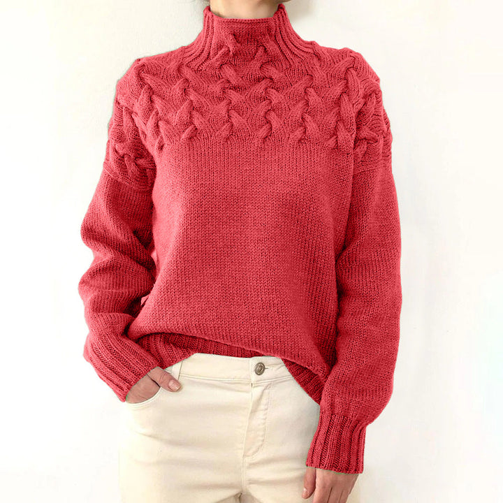 Front view of a model wearing a red cable knit mock neck sweater with cream trousers, hand in pocket