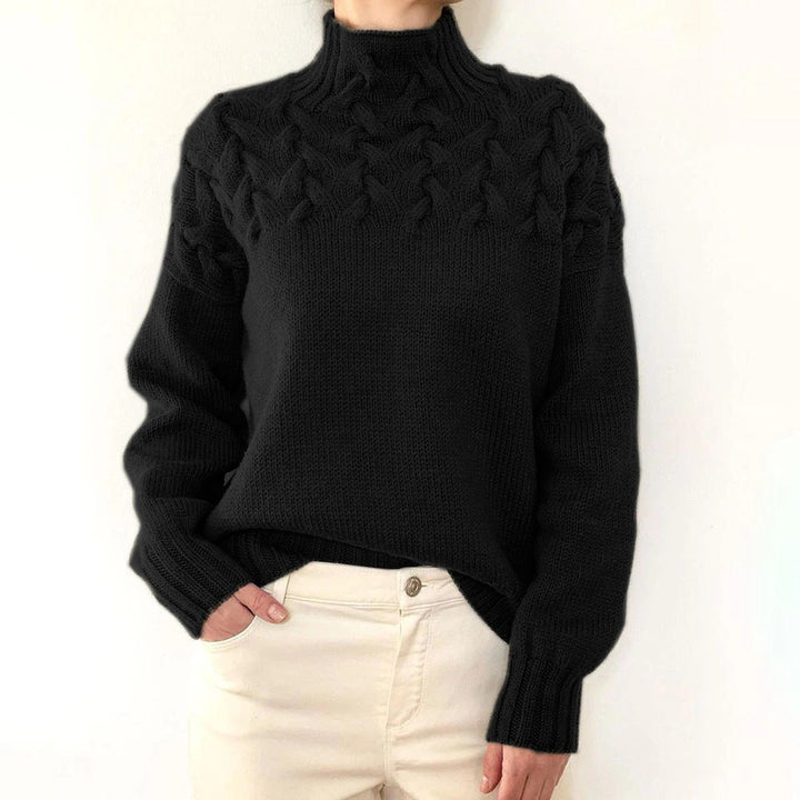 Front view of a model wearing a black cable knit mock neck sweater with cream trousers, hand in pocket