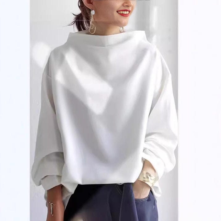 Front view of a model wearing a white oversized high neck sweater with a gold cuff bracelet and dark jeans