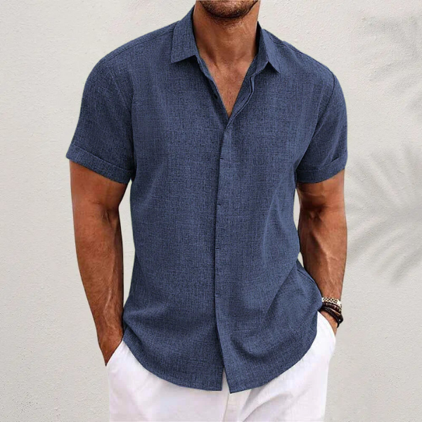 Front view of a man wearing a blue relaxed fit linen shirt with short rolled sleeves and white pants