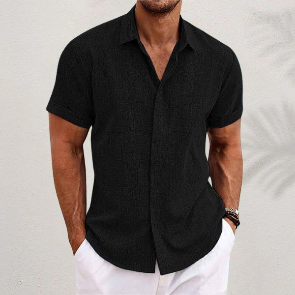 Front view of a man wearing a black relaxed fit linen shirt with rolled sleeves and white pants