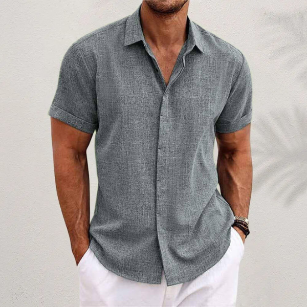 Front view of a man wearing a grey relaxed fit linen shirt with rolled sleeves and white pants