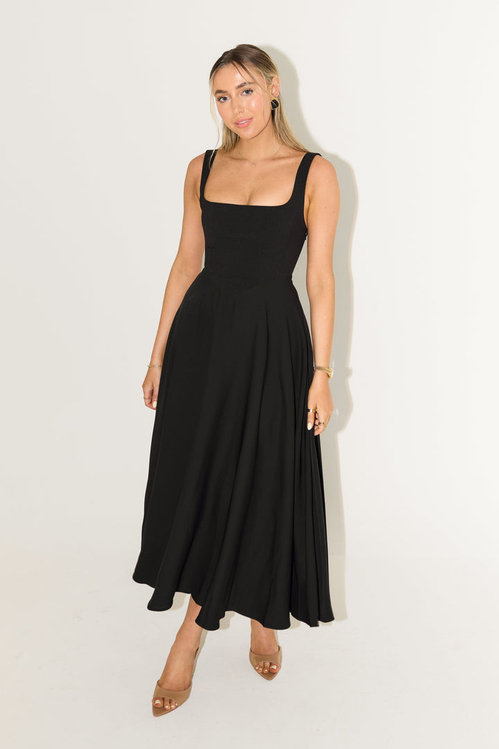 Front three quarter view of a model wearing a black timeless flowy midi dress with a square neckline