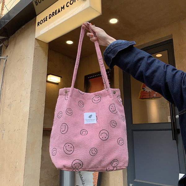 Pink smiley print corduroy tote bag held by a model in denim