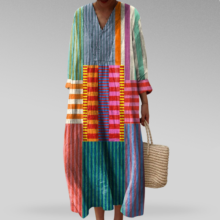 Patterned Kaftan Dress, front view worn by model, showing colourful stripes and a V-neckline, with a woven bag