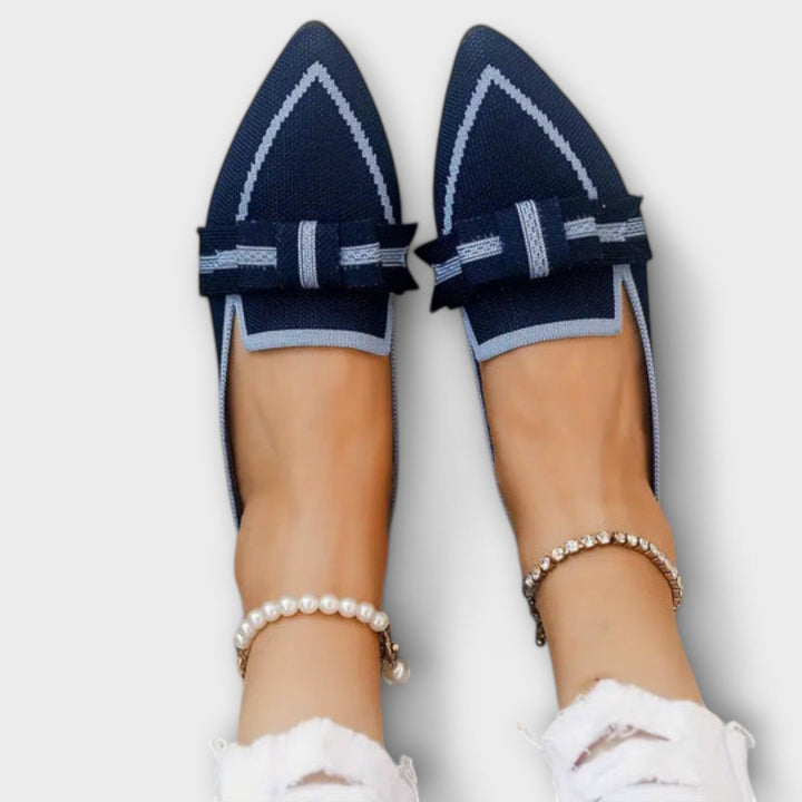 Top down view of a model wearing navy knotted flat loafer shoes with a pearl and a diamante anklet