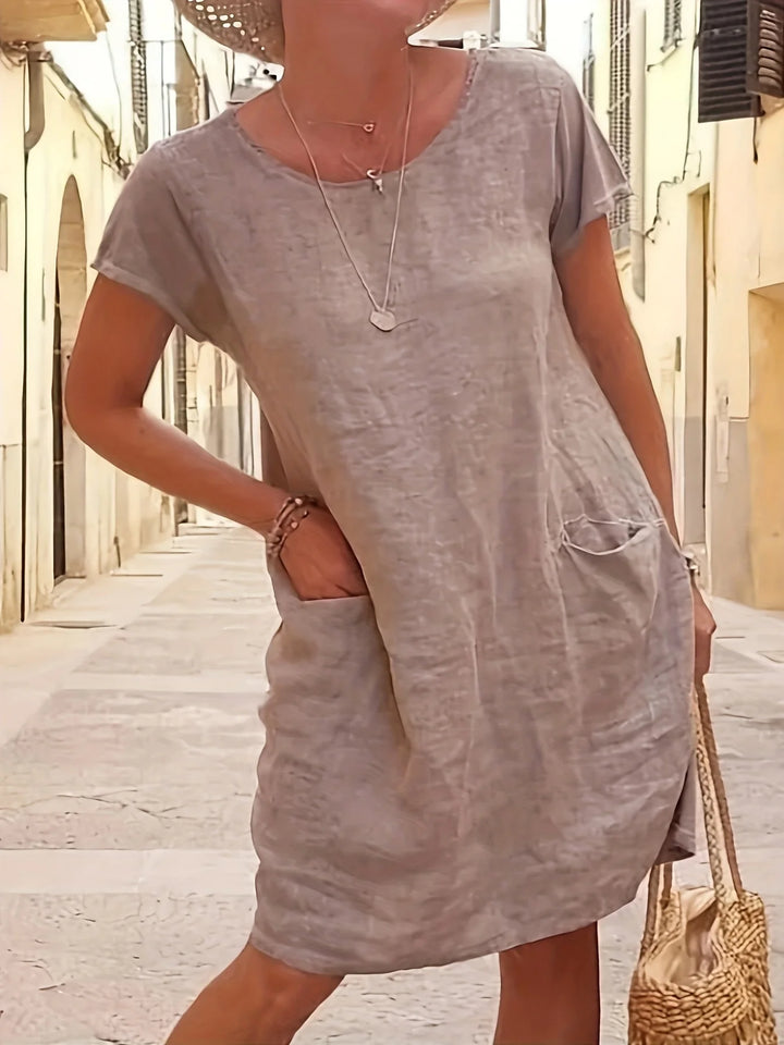 Front view of a grey loose cotton linen dress with short sleeves, round neck, and two side pockets