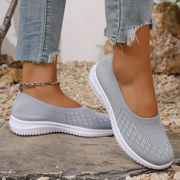 Three quarter view of a model wearing grey breathable mesh flats with white soles and ripped jeans