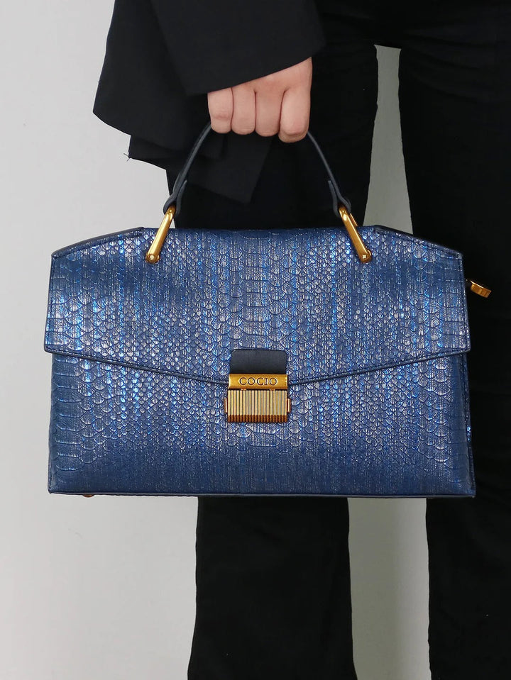 Front view of a model holding a blue Serpentina snake-print embossed vegan leather bag with gold hardware
