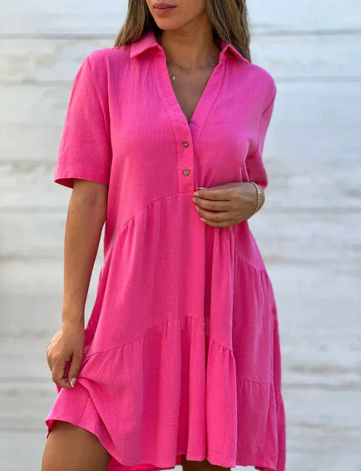 Close up of a model wearing a hot pink loose blouse mini dress with a collared V-neck and tiered skirt