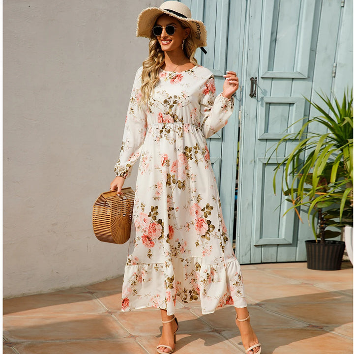 Front view, worn by model, a white bohemian chiffon maxi dress with pink floral print, straw hat, and heels