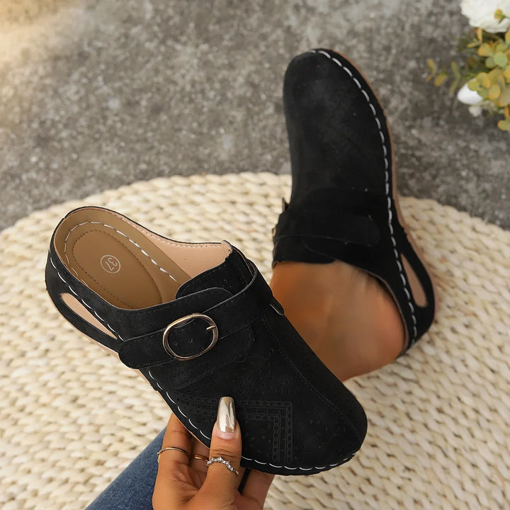 Close up of black orthopaedic summer slides with white stitching, one worn by model, one held by model