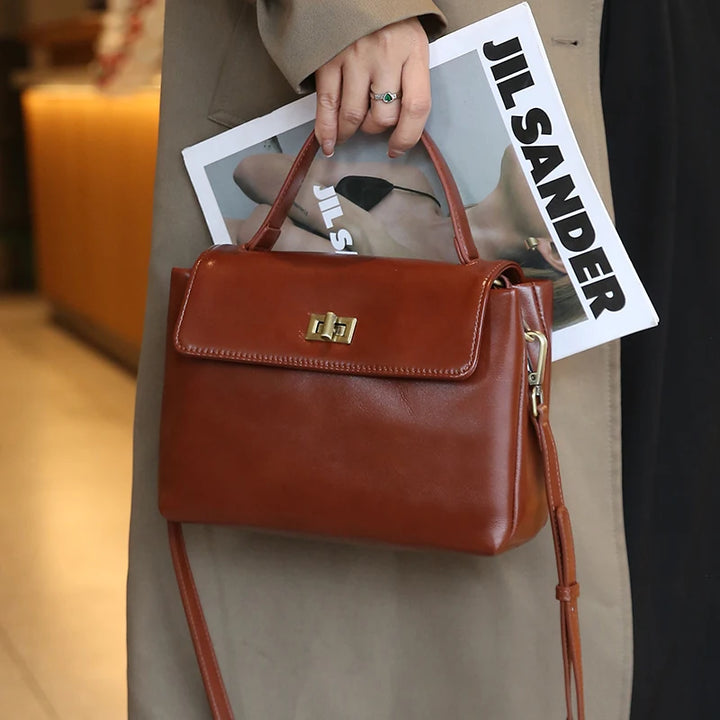 Worn by model, a brown Giselle leather tote bag held by a woman in a trench coat with a magazine